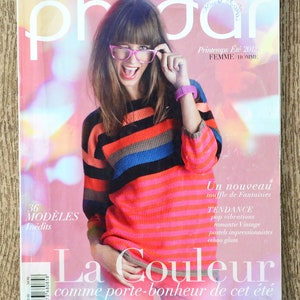 Puede incluir: Una portada de revista con una mujer que lleva un suéter a rayas de colores y gafas rosas. La revista se titula "Phildar" y el texto de la portada dice "Printemps Été 2012 FEMME/HOMME" y "Un nouveau souffle de Fantaisies TENDANCE pop vibrations romantic Vintage pastels impressionnistes ethno glam La Couleur comme porte-bonheur de cet été".