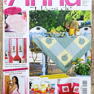 Op de afbeelding: Een tijdschriftcover met de roze titel "Anna" en de woorden "Idées de Déco d'été" eronder. De cover toont een gedekte tafel met een geruit tafelkleed en een mand met fruit. Het tijdschrift heet "Burda Ouvrages Manuels" en kost € 5,00.