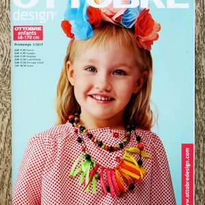 May include: A magazine cover with a girl wearing a floral headband and a beaded necklace with ribbon details. The cover reads "OTTOBRE design" and "Printemps 1/2017". The background is a light blue. The magazine is for children.