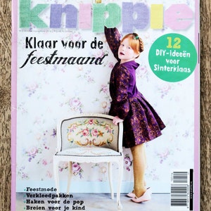 May include: A magazine cover with the title "KnipPie" in colorful letters. The cover features a young girl wearing a purple dress and holding a chair. The text "Klaar voor de feestmaand" is in large, bold letters. The magazine is for sizes 50 to 170.