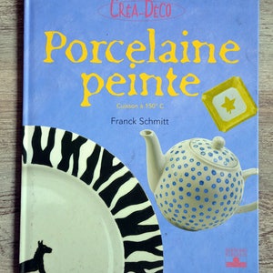 Puede incluir: Una portada de libro con el título "Porcelaine peinte" en letras amarillas sobre un fondo azul. El libro trata sobre la pintura en porcelana y presenta una tetera con lunares azules y un plato con rayas de cebra negras y blancas.