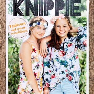May include: A magazine cover featuring the word "KNIPPIE" in large, black letters. Two girls are smiling and wearing floral print tops. The magazine cover also includes the text "9 patronen maal 134-176 en buidellasjes".