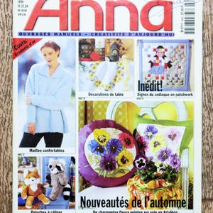 以下が含まれることがあります： 「アンナ」という赤い文字で書かれた雑誌の表紙。表紙には、刺繍、パッチワーク、かぎ針編みなど、さまざまなクラフトプロジェクトが掲載されています。表紙のテキストには、「Ouvrages Manuels - Creativite d'Aujourd'hui」と「Nouveautés de l'automne」と書いてあります。