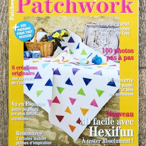 Op de afbeelding: Een tijdschriftcover voor "Pratique du Patchwork" met een kleurrijke quilt gemaakt van driehoekige stofstukken. De cover bevat ook de tekst "100 photos pas a pas" en "3D facile avec Hexifun".