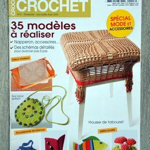 May include: A magazine cover featuring crochet projects, including a brown crocheted stool cover, a green crocheted bag, a blue crocheted bag, a red crocheted card holder, a colorful crocheted fish, and white crocheted mushrooms. The magazine cover is titled "Créations faciles au CROCHET" and features the text "35 modèles à réaliser".