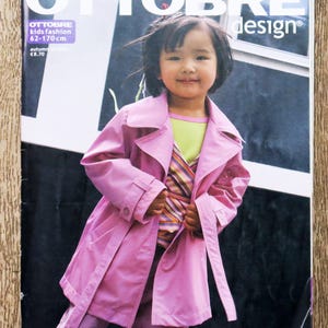 May include: A magazine cover with a child in a pink trench coat. The magazine is titled "OTTOBRE design" and includes text about kids' fashion, patterns, instructions, style, fashion, and quality. The magazine's size range is 62-170 cm.