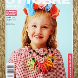 May include: A magazine cover showing a girl with a floral headband and a beaded necklace with ribbon details. The cover reads "OTTOBRE design" and "OTTOBRE kids fashion 68-170 cm". The background is a light blue.
