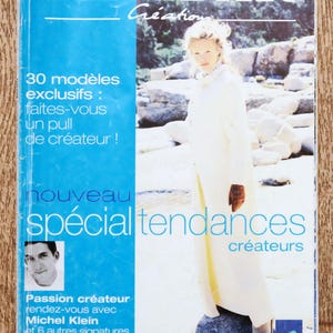 May include: Magazine cover with the title "PHILDAR Création" in white letters on a blue background. The cover features a woman in a white coat and the text "30 modèles exclusifs : faites-vous un pull de créateur!"