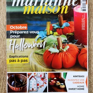 Peut inclure: Une couverture de magazine "marianne maison" avec un titre blanc et jaune. La couverture présente des citrouilles en tissu orange avec des tiges en bâtons de cannelle et le texte "Octobre, Préparez-vous pour Halloween".