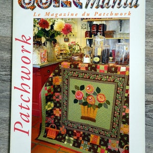 以下が含まれることがあります： パッチワーク雑誌「Quiltmania」の表紙。表紙には、花柄のキルトと花かごが描かれています。雑誌のタイトルは「Quiltmania」と「Le Magazine du Patchwork」。号数は53号、日付は2006年5月/6月です。