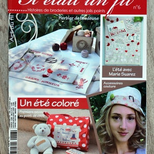 Peut inclure: Une couverture de magazine avec le titre "Il etait un fil" et le sous-titre "Histoires de broderies et autres jolis points". La couverture présente un sac en tissu à pois rouge et blanc avec un motif de point de croix d'une maison et le texte "Ma  bouse a bobos".