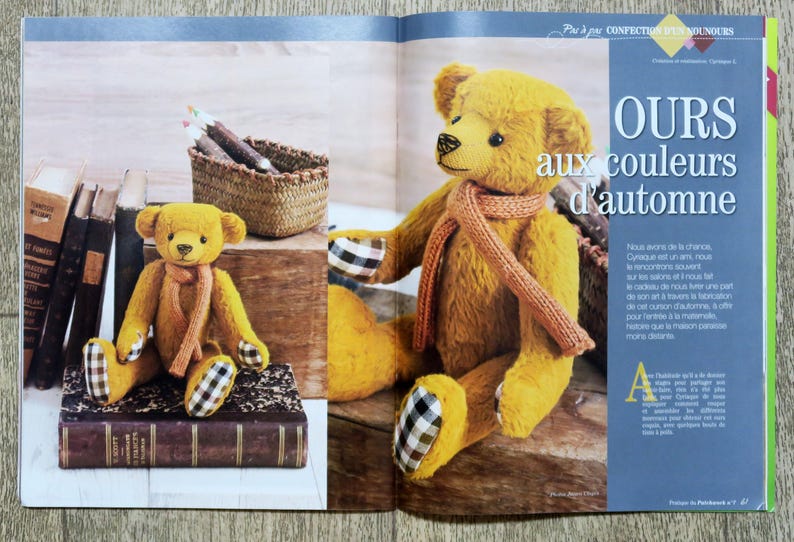 Op de afbeelding: Twee pluche teddyberen, een bruine en een gele, zijn gekleed in herfstthema outfits. De gele beer draagt een bruine sjaal en heeft een geruit patroon op zijn poten. De bruine beer draagt een geruite sjaal en heeft een geruit patroon op zijn poten. De tekst "OURS aux couleurs d'automne" is zichtbaar op de achtergrond.