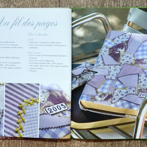 May include: A purple and white patchwork fabric book cover with the number "2005" stitched on it. The book is sitting on a metal chair.