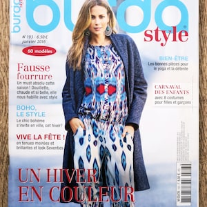 May include: A magazine cover featuring a woman wearing a blue and white patterned jumpsuit and a blue cardigan. The magazine is titled "Burda Style" and the cover text reads "Un hiver en couleur" which translates to "A winter in color".