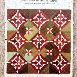 Peut inclure: Un patron de quilt imprimé intitulé "Swallows in the Window". Le motif présente un motif répétitif de formes géométriques rouges, blanches, vertes et marron, comprenant des étoiles et des diamants. Le texte "A respectful reproduction of an antique quilt" est également visible.