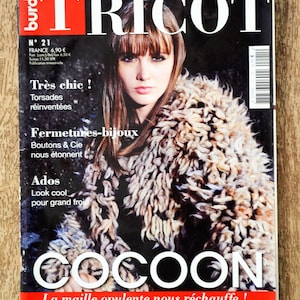Puede incluir: Una portada de revista con el título "TRICOT" en letras blancas grandes sobre un rectángulo rojo. La portada presenta a una mujer con un abrigo texturizado beige y marrón. La palabra "COCOON" se muestra de forma destacada, y el texto "Hiver 2012" está en la parte superior.