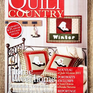 Könnte beinhalten: Ein Magazin-Cover mit dem Titel "QUILT COUNTRY" mit Winter-Quilting-Projekten. Das Cover zeigt Bilder von Kissen, Wandbehängen und einem dekorativen Stiefel, alle mit Winterthema. Das Magazin enthält auch den Text "Home sweet home".