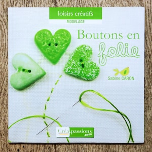 Op de afbeelding: Boekomslag met drie hartvormige groene knopen met knoopsgaten. De titel "Boutons en folie" staat in cursief. Het boek is voor creatieve hobby's en modellering, met de naam van de auteur, Sabine CARON.