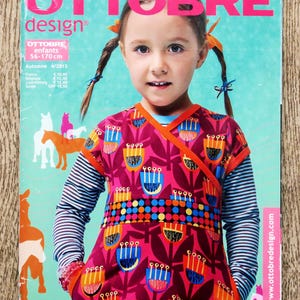 May include: The cover of an "OTTOBRE design" magazine shows a girl in a patterned wrap top and striped long-sleeved shirt. The magazine title is in pink, with the issue's title and size range (56-170cm) also visible.