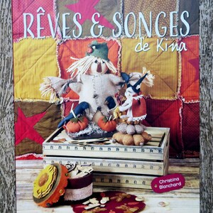 May include: A book cover with a patchwork background featuring a scarecrow, a witch, and pumpkins. The title of the book is "Rêves & Songes de Kina" by Christina Blanchard. The book is published by Les Editions de Saxe.
