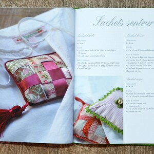 May include: A book with instructions on how to make scented sachets. The book is open to a page showing a pink and white striped sachet with a green trim and a small, round, gold button. The text on the page reads " Sachets senteur" and "Sachets beige".