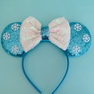 May include: Blue sequin Minnie Mouse ears with a white bow and snowflake embellishments.