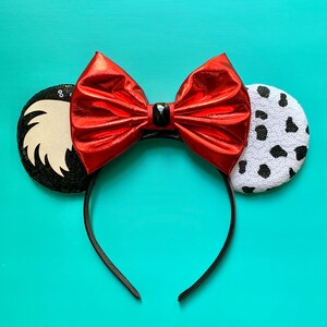 May include: Red, white, and black sequined Minnie Mouse ears with a red bow and a black gem in the center.