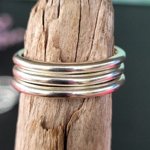 Puede incluir: Un conjunto de cuatro anillos de plata apilados uno encima del otro. Los anillos son lisos y brillantes.