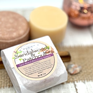 May include: A white paper wrapped bar of sandalwood and patchouli scented shampoo. The label reads "Sandalwood & Patchouli Earth Mineral Moisturizing Shampoo" and lists the ingredients. The bar weighs 3 ounces.