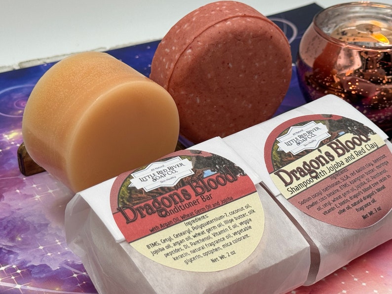 May include: Two round bars of soap, one red and one orange, wrapped in white paper with a red and white label that says "Dragon's Blood Conditioner Bar with Argan Oil, Wheat Germ Oil and Jojoba" and "Dragon's Blood Shampoo with Jojoba and Red Clay".