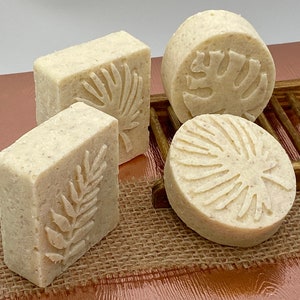 May include: Four handmade soap bars with a natural, off-white color. Each bar features a different embossed design of a tropical leaf.