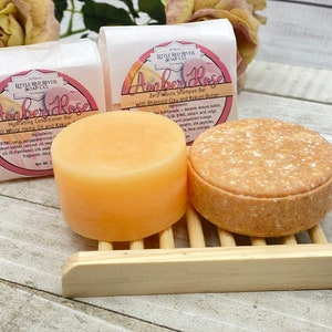May include: Two bars of soap, one orange and one brown, on a wooden soap dish. The bars are labeled "Amber Rose" and are zero waste shampoo and conditioner bars.