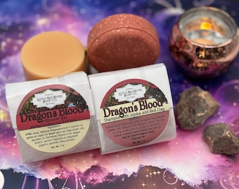 May include: Two bars of soap, one red and one beige, with the label "Dragon's Blood" and the text "All Natural Little Red River Soap Co."  The red bar is labeled "Shampoo with Jojoba and Red Clay" and the beige bar is labeled "Conditioner Bar with Argan Oil, Wheat Germ Oil and Jojoba".