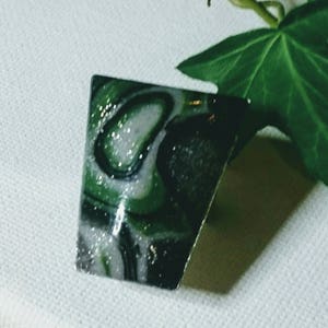 Puede incluir: Un anillo verde, negro y blanco con un diseño marmoleado y purpurina plateada.