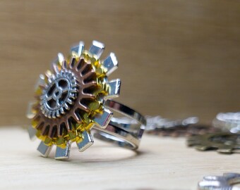Puede incluir: Un anillo de plata con un gran diseño de engranaje multicolor. El engranaje está hecho de metal plateado, dorado y cobre. El anillo es ajustable.