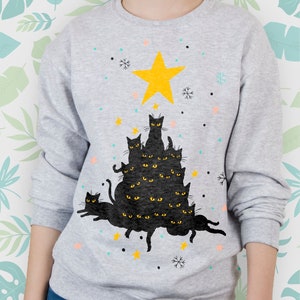 May include: A gray sweatshirt with a black cat Christmas tree design. The tree is made up of multiple black cats stacked on top of each other, with a yellow star on top. The cats have yellow eyes and are arranged in a tree shape.