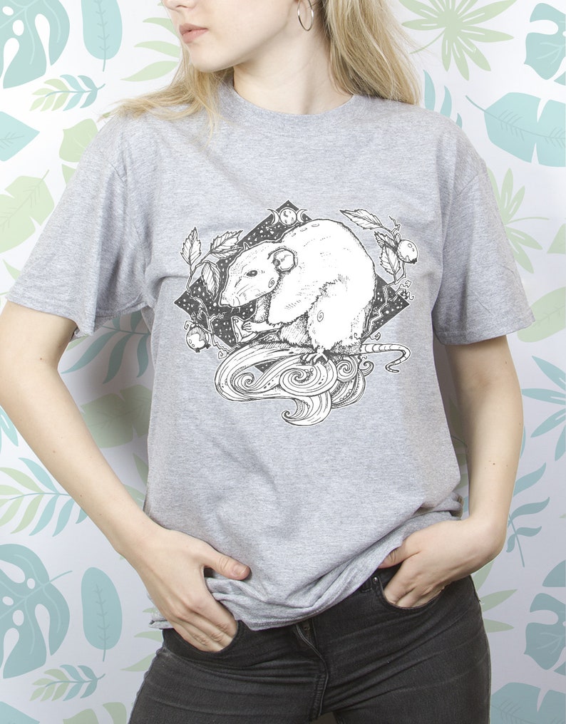 May include: A gray t-shirt with a black and white illustration of a rat with a swirling tail and leaves. The rat is surrounded by a black diamond shape with a moon and stars inside.