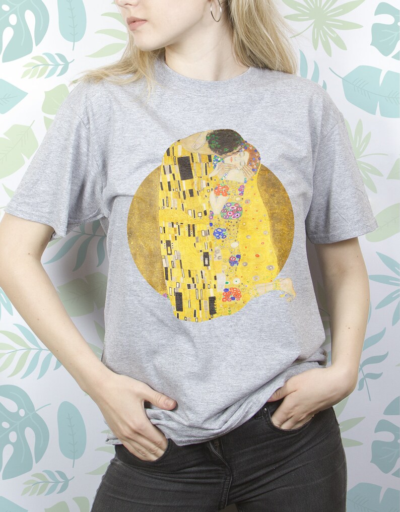May include: A gray t-shirt with a print of Gustav Klimt's "The Kiss" painting. The painting features two figures embracing in a golden, mosaic-like design.