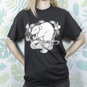 May include: Black t-shirt with a white graphic print of a rat with a crescent moon and stars. The rat is surrounded by leaves and vines.