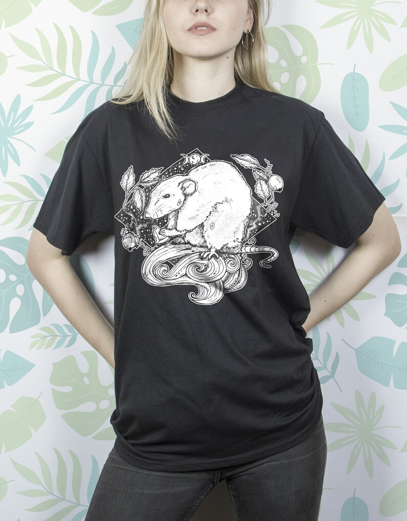 May include: Black t-shirt with a white graphic print of a rat with a crescent moon and stars. The rat is surrounded by leaves and vines.