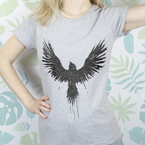May include: A grey t-shirt featuring a black silhouette of a bird with outstretched wings. The bird is stylised with a dripping paint effect.