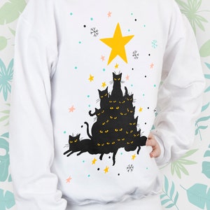May include: White sweatshirt with a black cat Christmas tree design. The cats are stacked on top of each other, forming a tree shape. A yellow star is at the top of the tree.