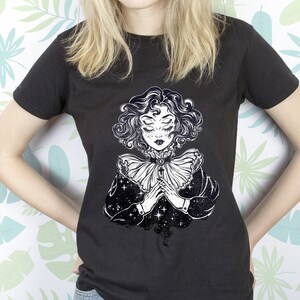 May include: Black t-shirt with a white graphic print of a woman with closed eyes and a starry background.