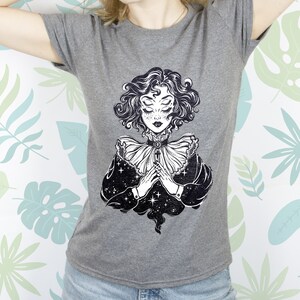 May include: Gray t-shirt with a black and white illustration of a woman with multiple eyes and a star-filled sky behind her.
