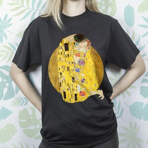 May include: A black t-shirt with a graphic print of Gustav Klimt's "The Kiss" painting. The painting features two figures embracing in a golden, mosaic-like style.