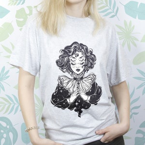 May include: A gray t-shirt with a black and white illustration of a woman with multiple eyes and a star-filled background.