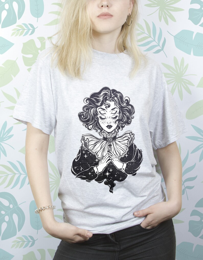 May include: A gray t-shirt with a black and white illustration of a woman with multiple eyes and a star-filled background.