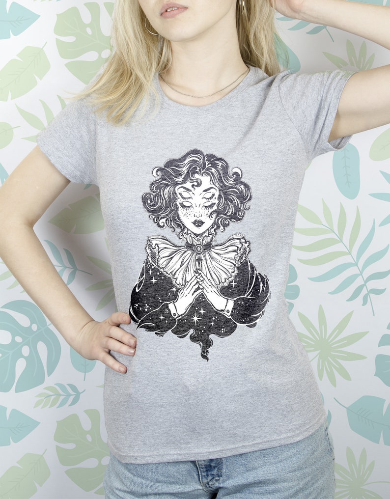 May include: Gray t-shirt with a black and white illustration of a woman with closed eyes and a star-filled background.