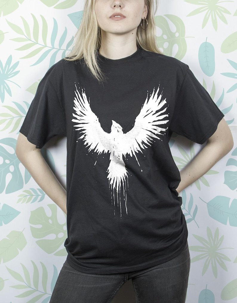 May include: Black t-shirt featuring a white graphic of a bird with its wings outstretched.