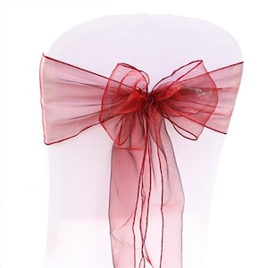 Puede incluir: Falda de silla de color burdeos hecha de tela de organza transparente, atada en un lazo en la parte posterior de una silla blanca.